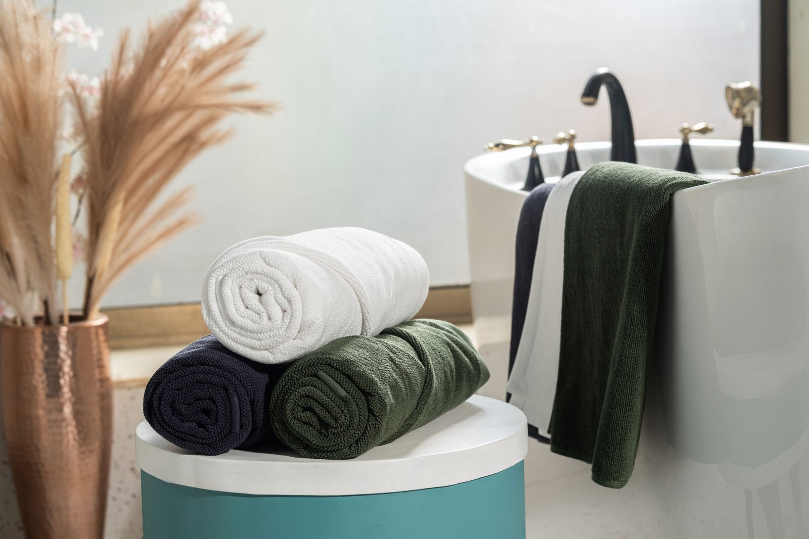 White, Green and Blue towels rolled and placed on a side table near a bathtub